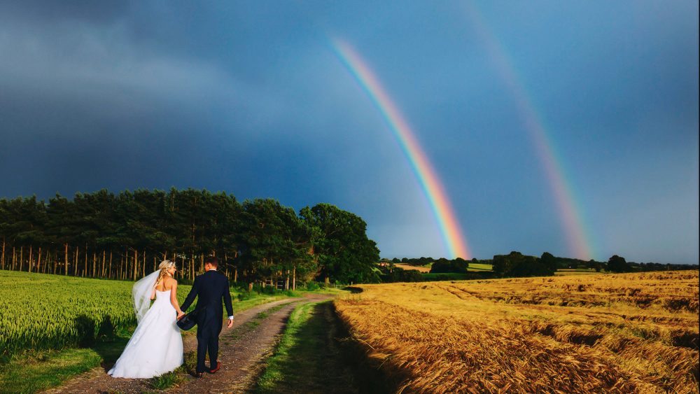 wedding couple walking toward a double rainbow