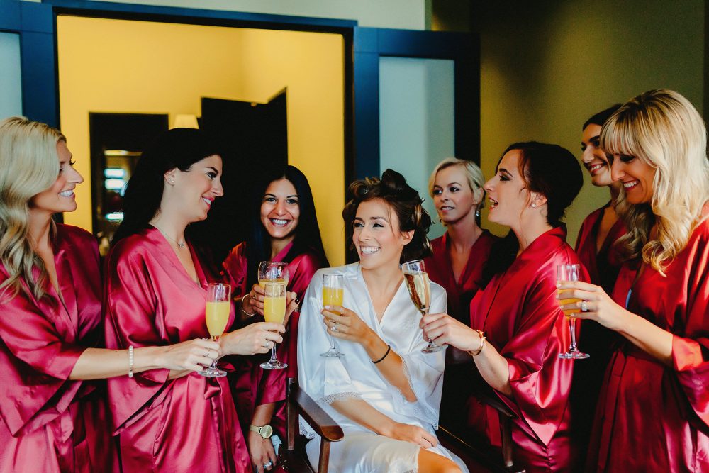 bride and bridesmaids laughing and drinking champagne before wedding