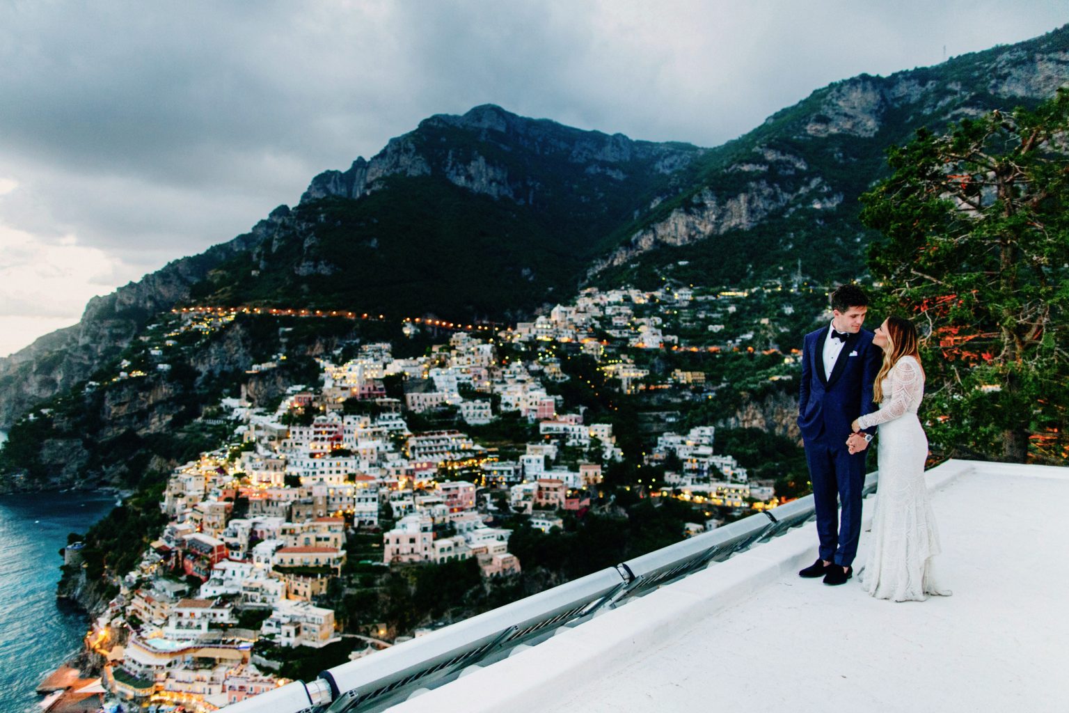 Bride and groom embrace on a rooftop overlooking a city.