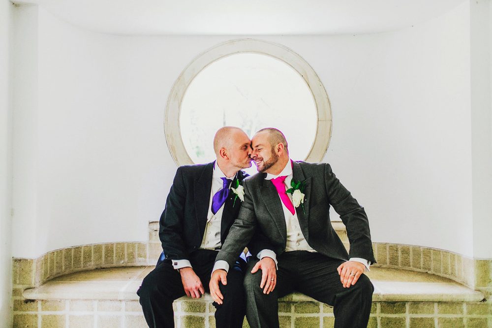 Two grooms kiss in front of circular window