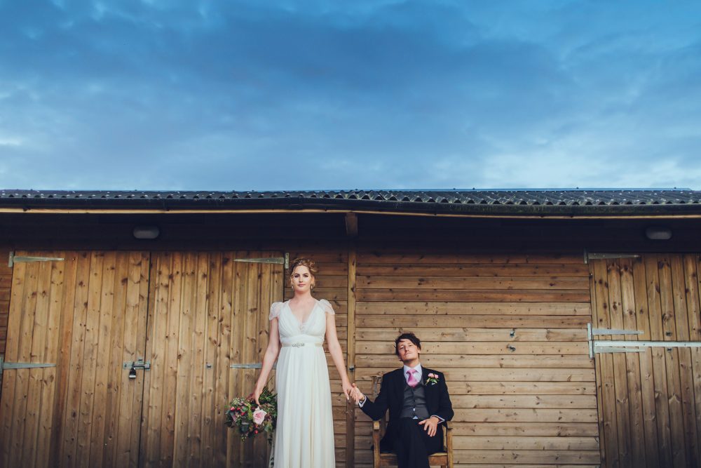 quirky wedding portrait with bride standing and groom sitting
