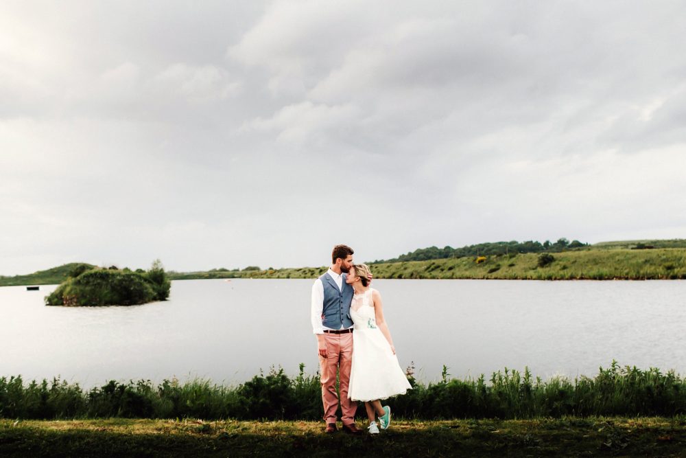 groom and bride embrace next to a lake