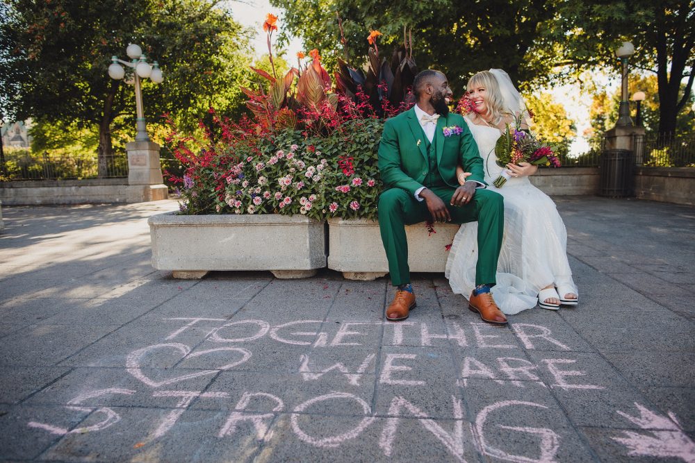 bride and groom laughing next to the words Together We Are Strong" written in chalk on the ground